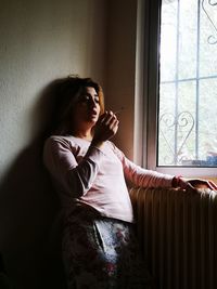 Young woman sitting by window at home