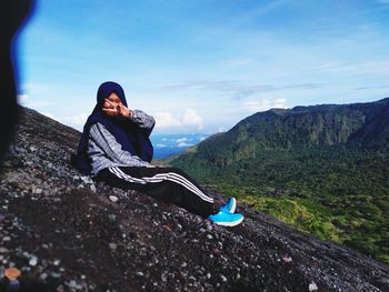 Young woman sitting on mountain against sky