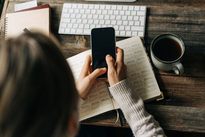 Top view of desktop where unrecognizable woman is using mobile phone and organizer for work.