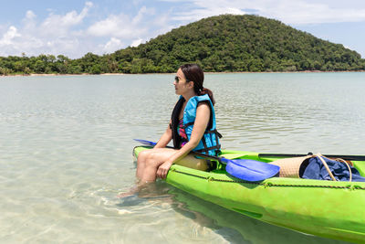 Portrait of smiling young woman sitting on kayak in the sea against sky