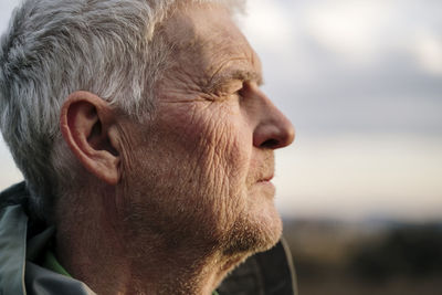 Senior man with wrinkled face against during sunset