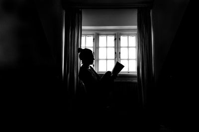 Side view of woman reading book by window