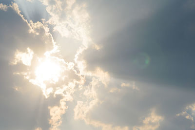 Low angle view of sunlight streaming through clouds
