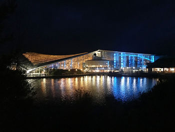 Illuminated buildings by river against sky at night