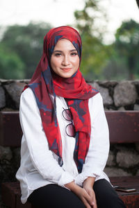 Portrait of smiling young woman wearing hijab while sitting on bench