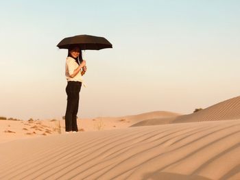 Woman standing on sand dune in desert against sky