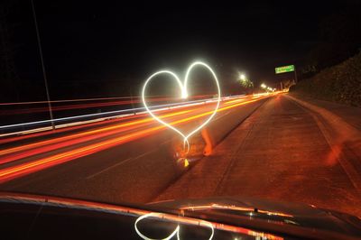 Blurred motion of woman and heart shape light painting on road seen through car windshield at night