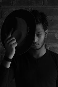 Portrait of young man holding hat against wall