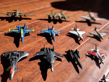 Rows of snall toy military planes arranged on a hardwood floor, casting shadows.