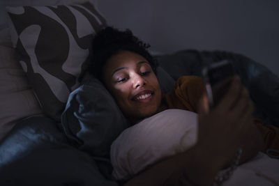 Smiling young woman using phone in bed