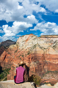 Rear view of woman sitting on rock against sky