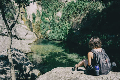 Rear view of woman sitting on rock by river