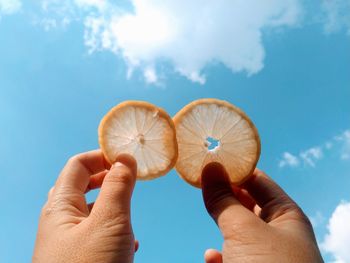 Close-up of person holding lemon slices  against sky background