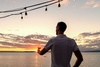 Rear view of man looking at sea against sky during sunset