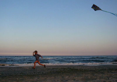 Full length of boy playing with kite at beach during sunset