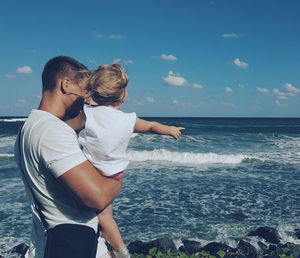 Father carrying daughter while standing at beach