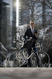 Grey-haired businessman with bicycle and coffee to go in the city