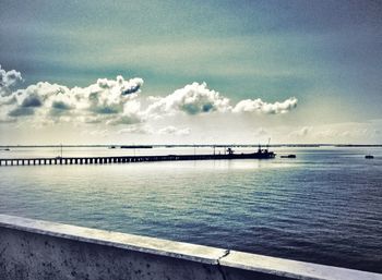 Pier on sea against cloudy sky