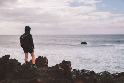 Woman standing on rocks by sea against sky