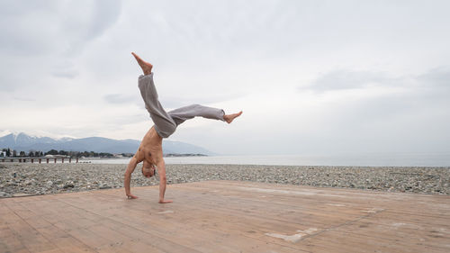 Full length of woman jumping at beach against sky