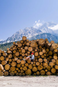 Woman sitting on the stack of the tree logs