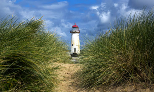 Lighthouse amidst grass and buildings against sky