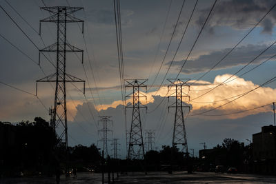 Low angle view of silhouette electricity pylons against sky at sunset