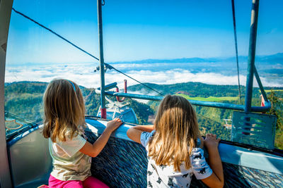 Girls traveling in overhead cable car against sky