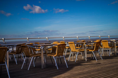 Empty chairs and table at beach against blue sky