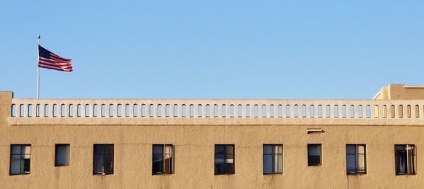 Low angle view of flag against building against clear blue sky