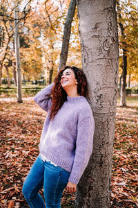 Young woman smiling while sitting on tree trunk during autumn