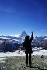 Rear view of woman standing on snowcapped mountain against sky