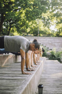 Side view of male and female friends practicing push-ups on steps