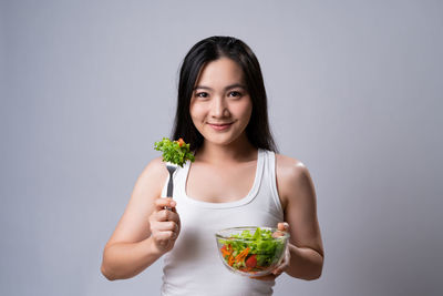 Portrait of smiling woman holding ice cream against gray background