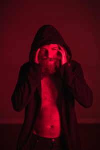 Close-up of young man wearing hooded jacket with headache standing in illuminated room