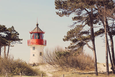 Lighthouse amidst trees and buildings against sky