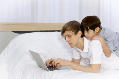 Rear view of woman using mobile phone while sitting on bed