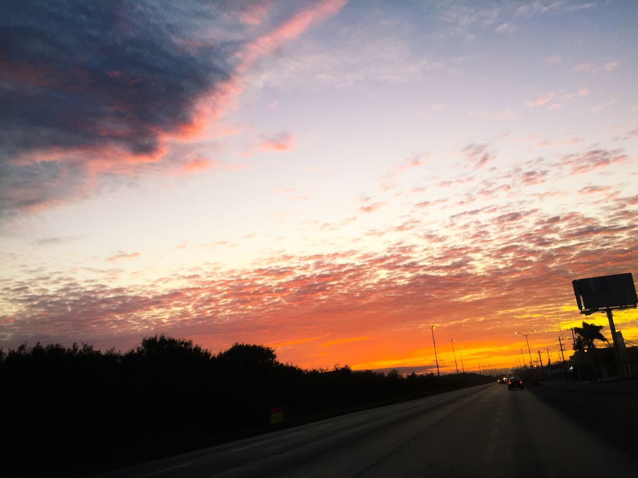 ROAD BY SILHOUETTE CITY AGAINST ORANGE SKY