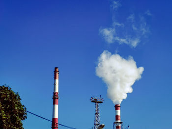 Low angle view of smoke emitting from factory against blue sky