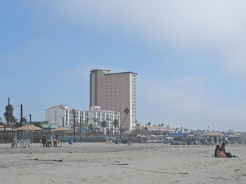 People on beach by buildings against sky