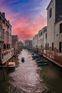 Boats in canal amidst buildings against sky during sunset