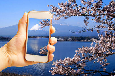 Close-up of hand holding flower over lake against sky