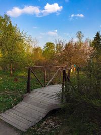 Wooden railing on footpath by trees against sky