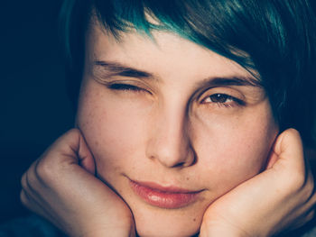 Close-up portrait of woman winking against black background