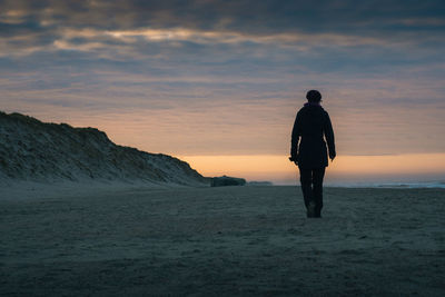 Rear view of woman walking at beach against sky