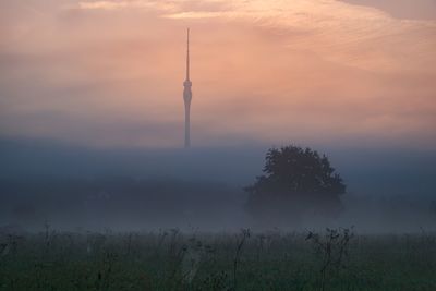 Communications tower on field against sky during sunset