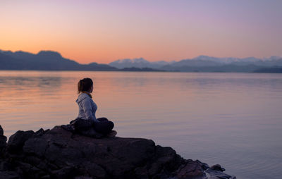 Man sitting on rock against sky during sunset