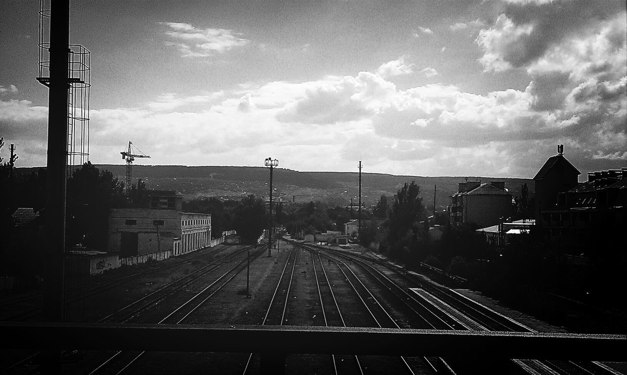 transportation, building exterior, architecture, sky, built structure, railroad track, city, cloud - sky, the way forward, mode of transport, road, diminishing perspective, vanishing point, land vehicle, public transportation, road marking, rail transportation, cloud, car, city life