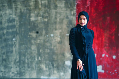 Portrait of young woman standing against wall