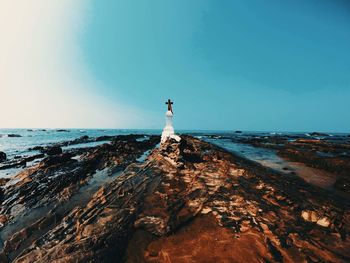 Man standing on rock by sea against clear sky